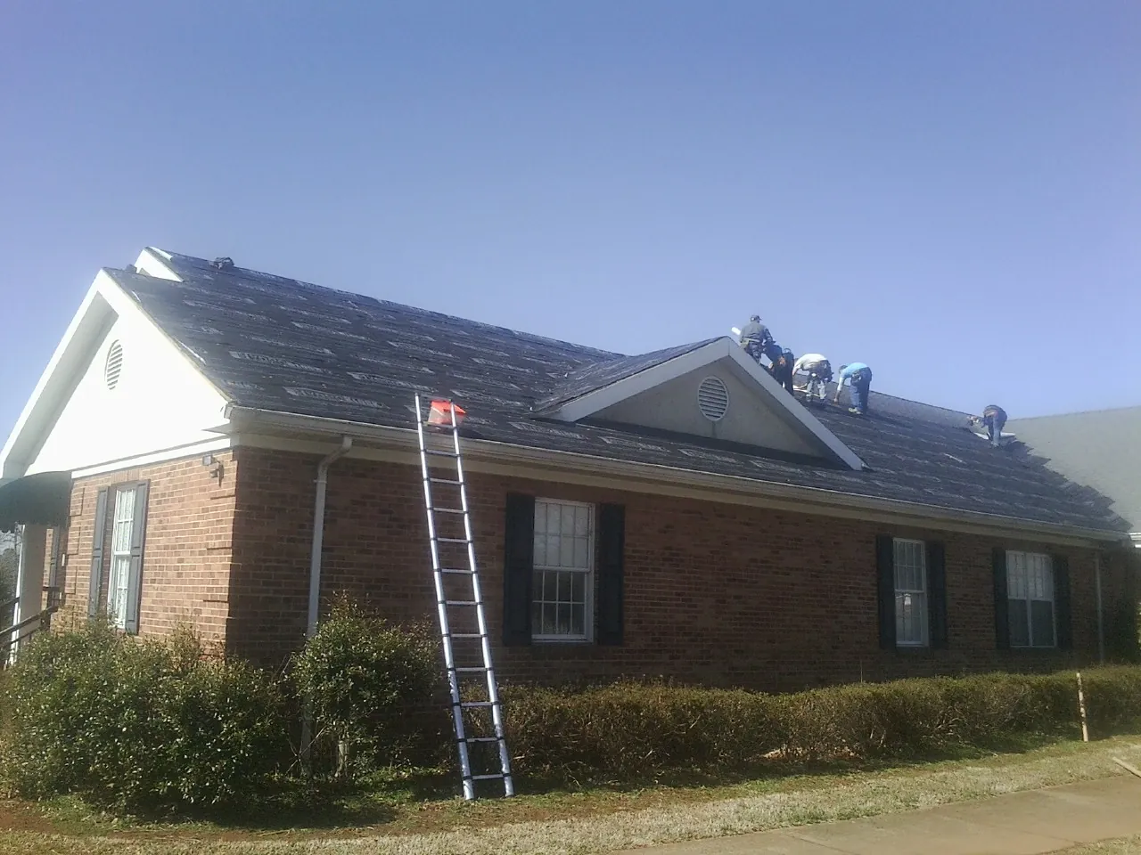 Crew tearing shingles off a brick ranch roof with a ladder set — Metal Roof Repair work by our crew in Bingham Canyon
