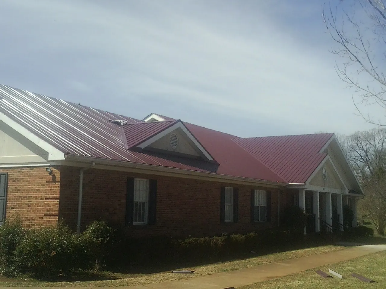 Red metal roof with gabled entries on a long brick building, from a Hail Damage Roof Repair job in Bingham Canyon