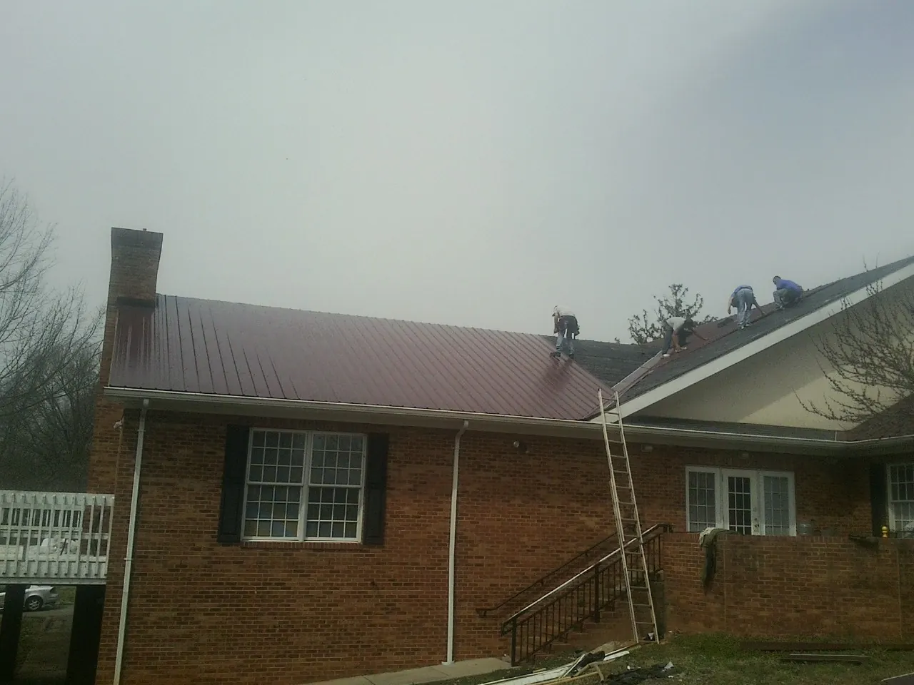 Crew setting red metal roofing panels on a brick home in Bingham Canyon