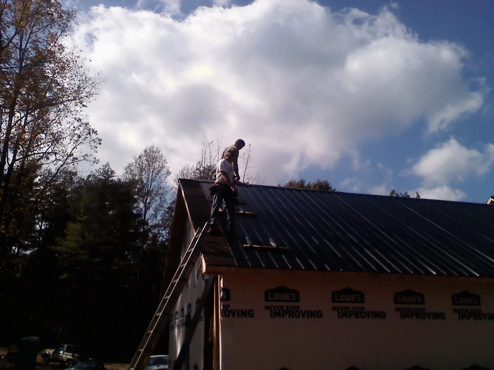 Roofer fastening dark metal panels high against a cloudy sky, from a Roof Inspection job in Bingham Canyon