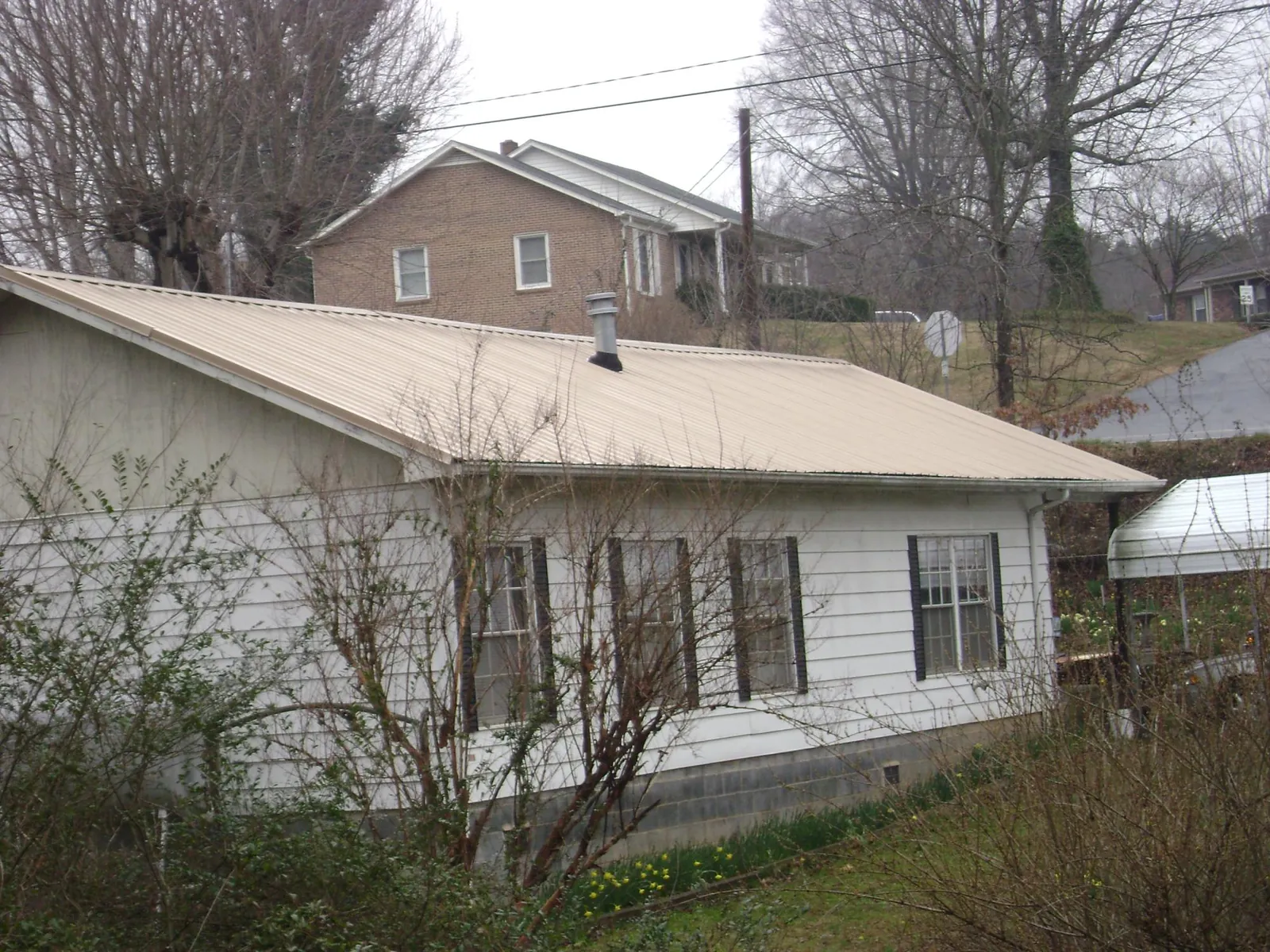 Tan metal roof on a white sided house set into a hillside — Commercial Roofing by Roofing Brothers in Bingham Canyon