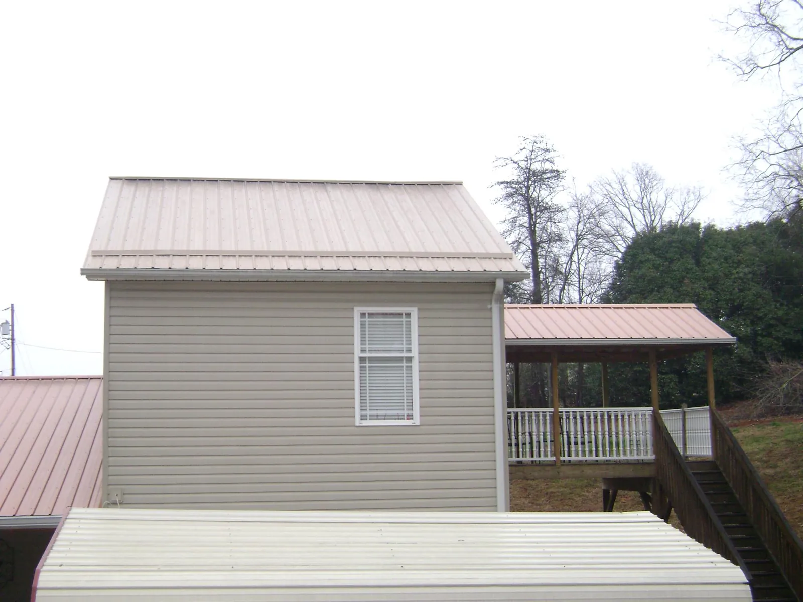 Tan metal roofs on a two story addition and attached porch, from a Roof Replacement job in Bingham Canyon